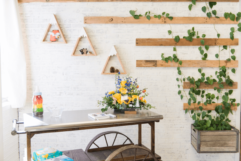 Woodland-themed baby boy shower guest book table set up on a wooden cart and adorned with a blue and yellow flower arrangement.