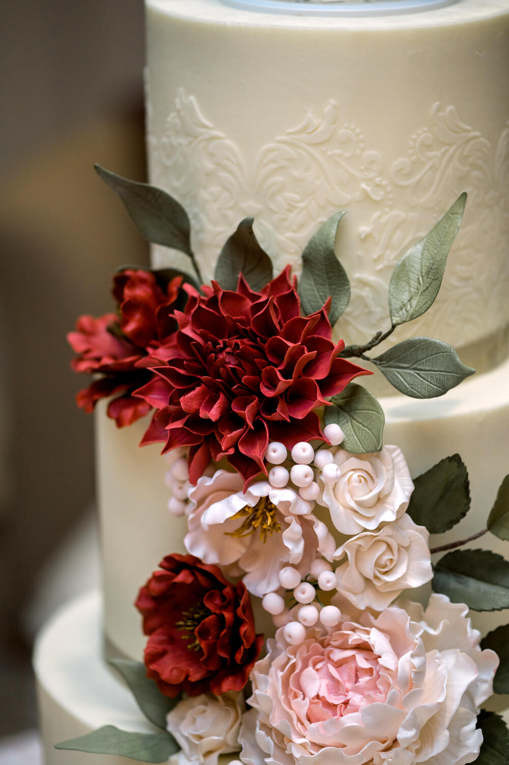 Celebrating 50 Years of Love: Our Parents' Golden Anniversary 27 Detailed view of handcrafted sugar flowers in blush and burgundy on a white buttercream cake for a 50th wedding anniversary celebration.