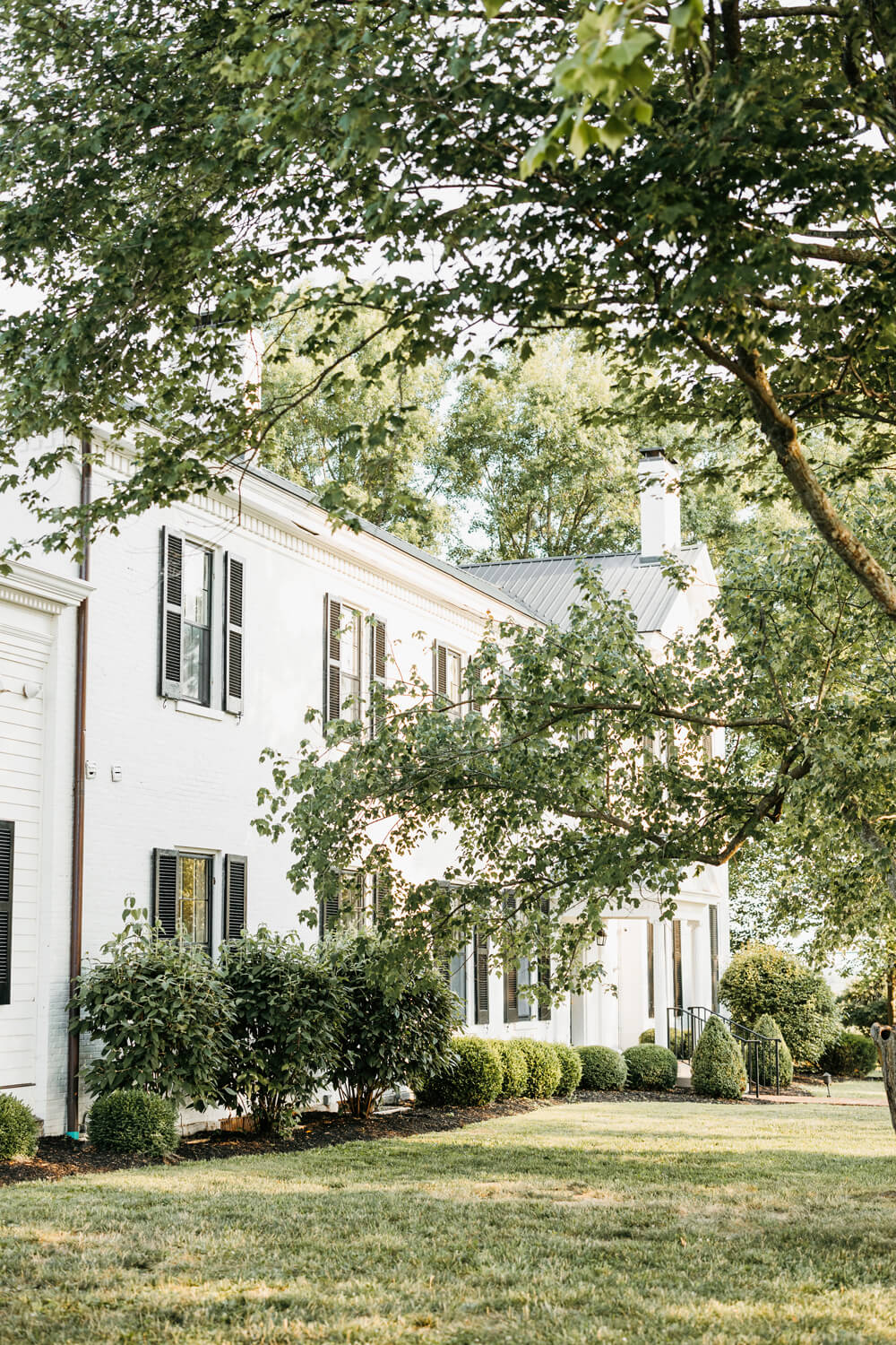 Black and White Wedding Invitations for a Classic Ashford Acres Inn Wedding 2 Exterior view of the historic white mansion at Ashford Acres Inn, surrounded by lush greenery and mature trees on a sunny day.