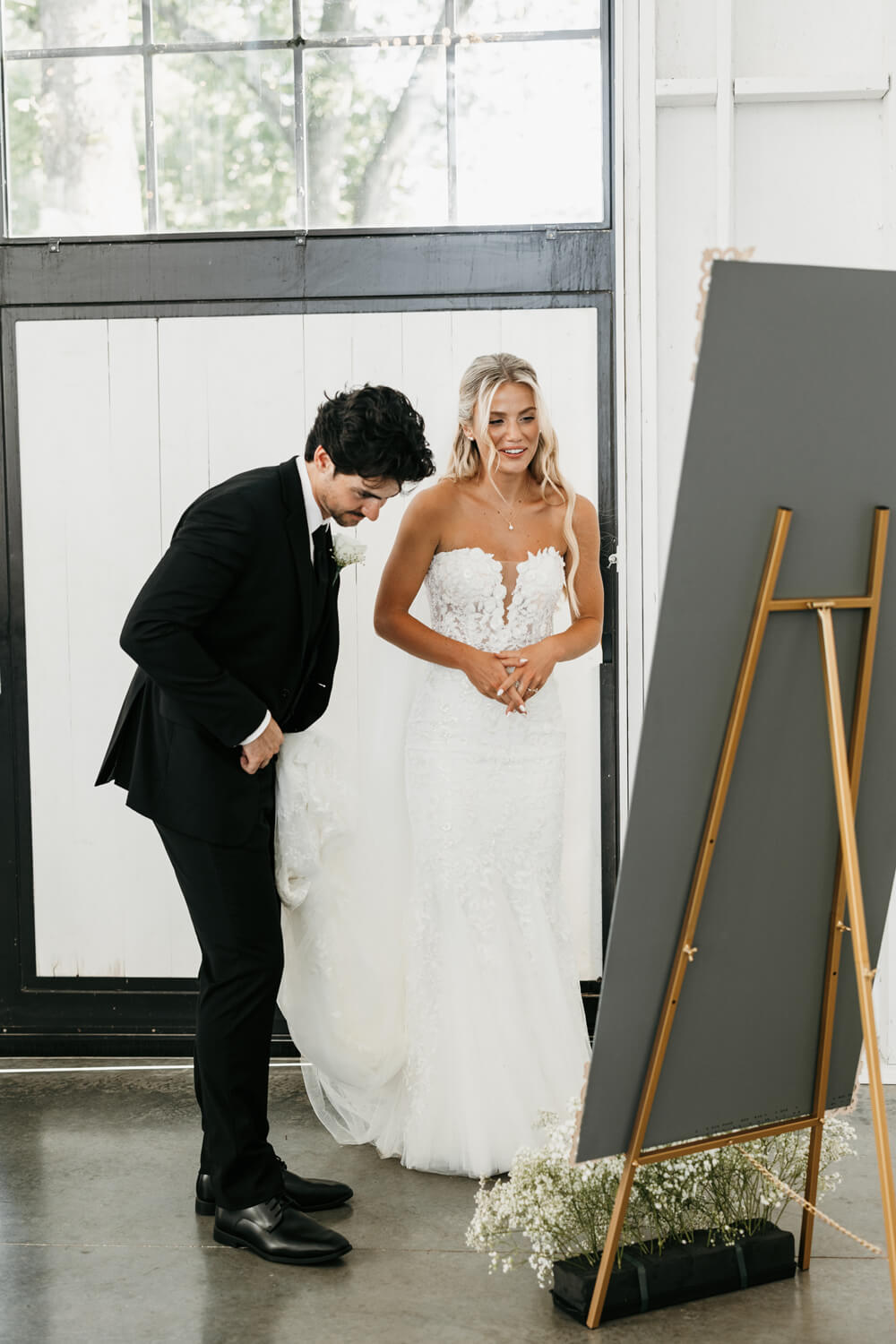 Black and White Wedding Invitations for a Classic Ashford Acres Inn Wedding 27 Audrey and Nathaniel smiling as they look at their custom mirror seating chart during their Ashford Acres Inn reception.