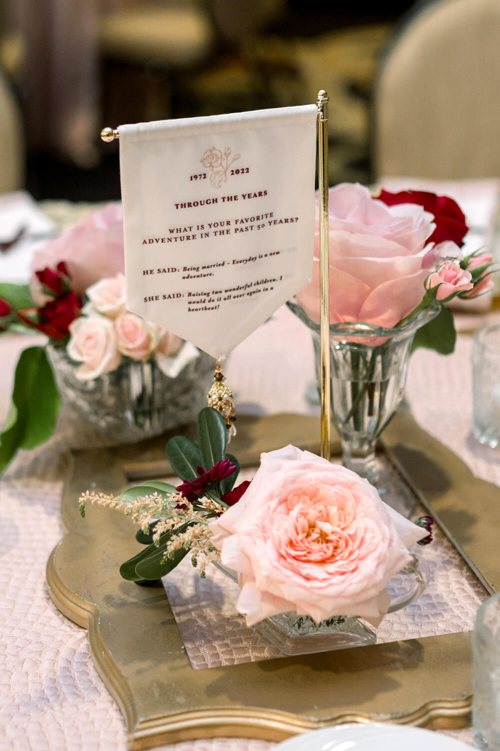 Celebrating 50 Years of Love: Our Parents' Golden Anniversary 14 50th anniversary table centerpiece with blush and burgundy roses in crystal bud vases, in a vintage gold frame.