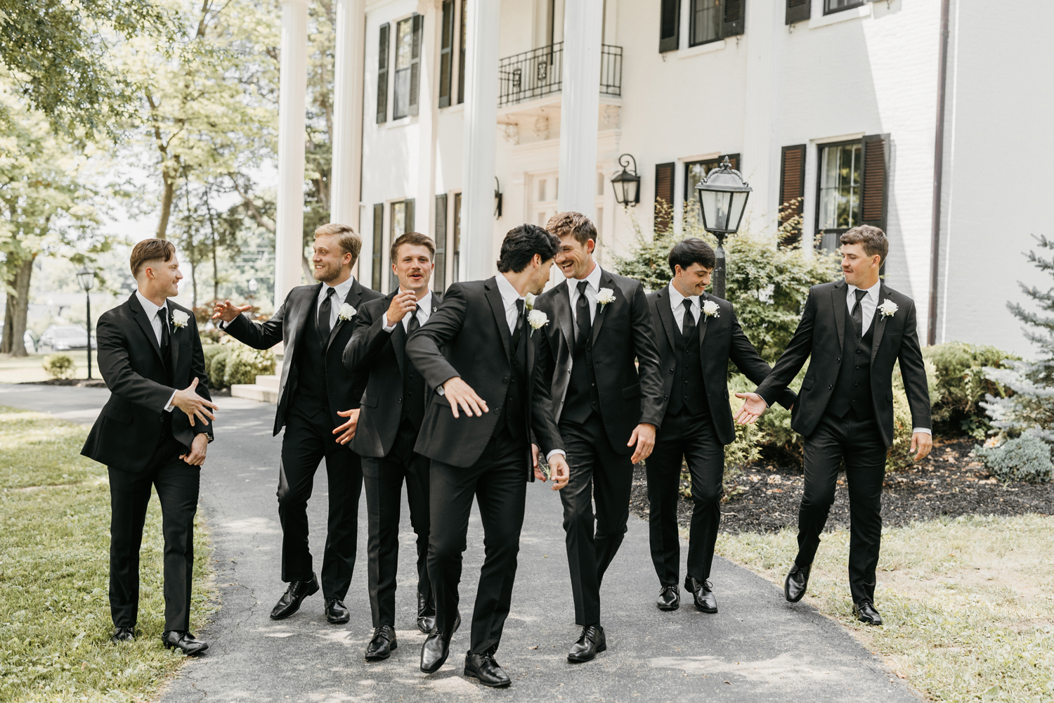 Black and White Wedding Invitations for a Classic Ashford Acres Inn Wedding 9 Groomsmen in black suits laughing and walking together in front of Ashford Acres Inn’s white-columned mansion.