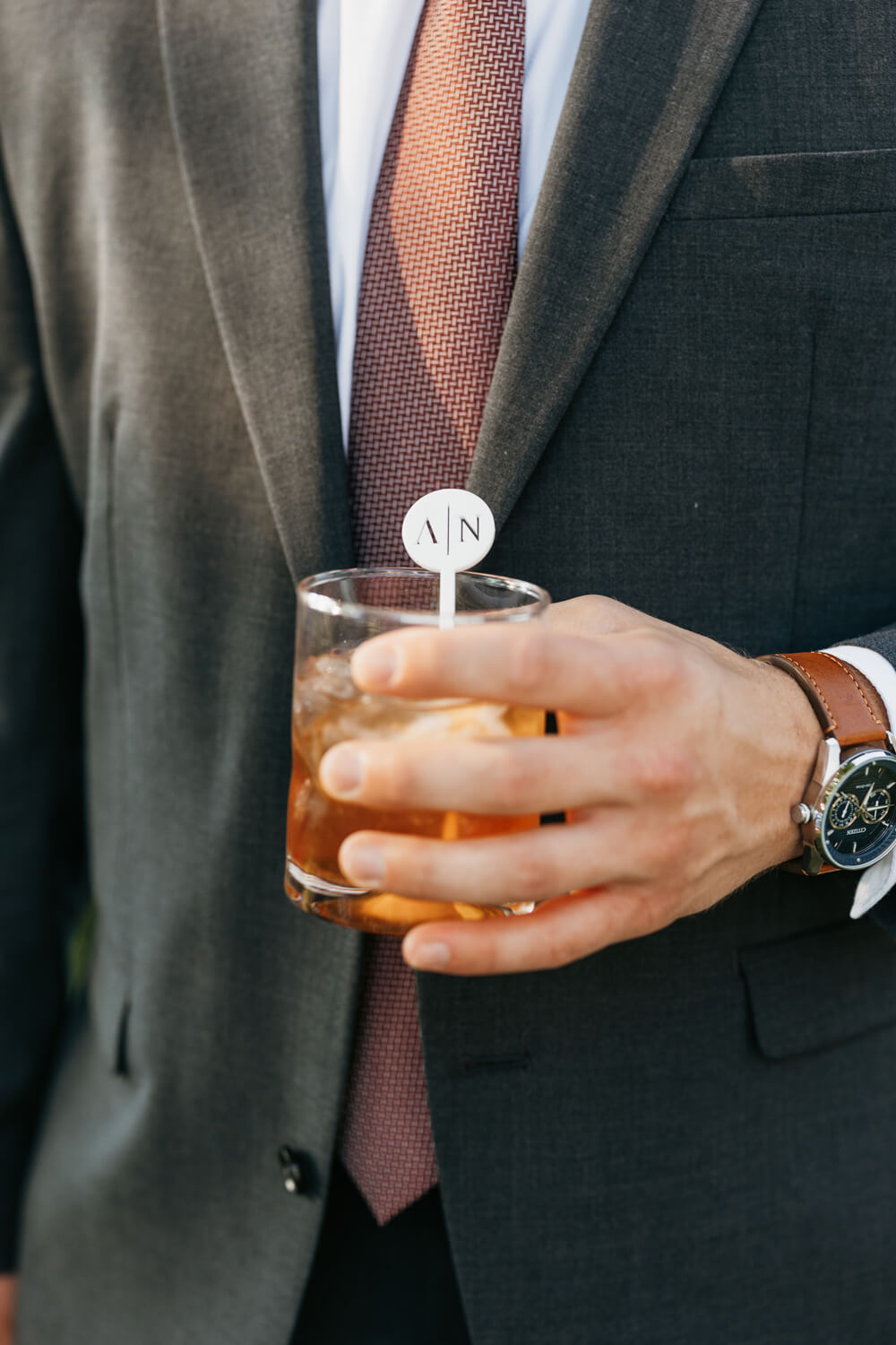 Black and White Wedding Invitations for a Classic Ashford Acres Inn Wedding 24 Guest in a suit holding an old fashioned cocktail with a personalized “A | N” drink stirrer, styled to match the black and white wedding theme.