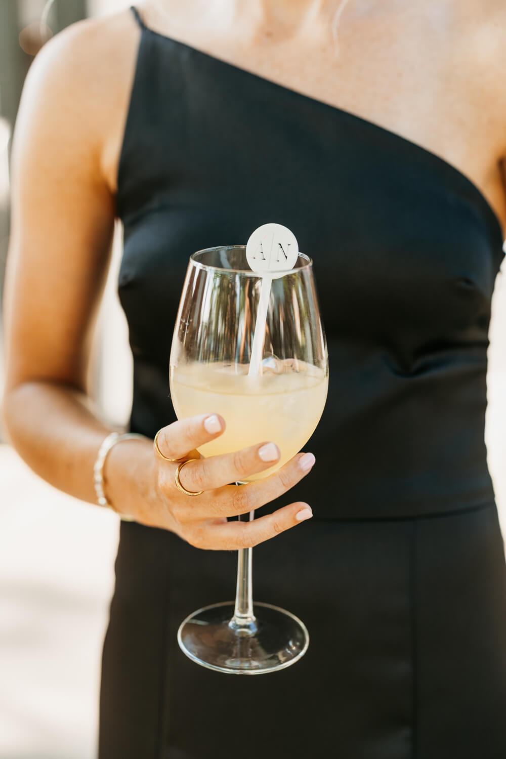 Black and White Wedding Invitations for a Classic Ashford Acres Inn Wedding 25 Bridesmaid holding a peach sangria in a stemmed glass with a custom monogrammed “A | N” drink stirrer, wearing a black one-shoulder dress.
