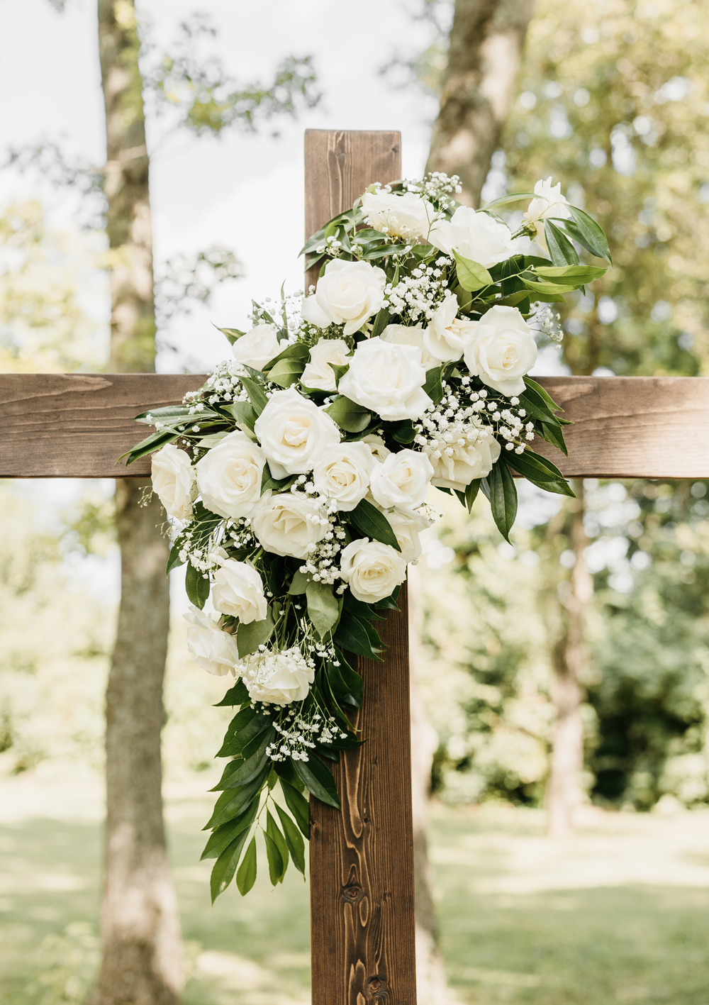 Black and White Wedding Invitations for a Classic Ashford Acres Inn Wedding 13 Ceremony cross decorated with white roses, baby’s breath, and greenery, set against trees at Ashford Acres Inn.