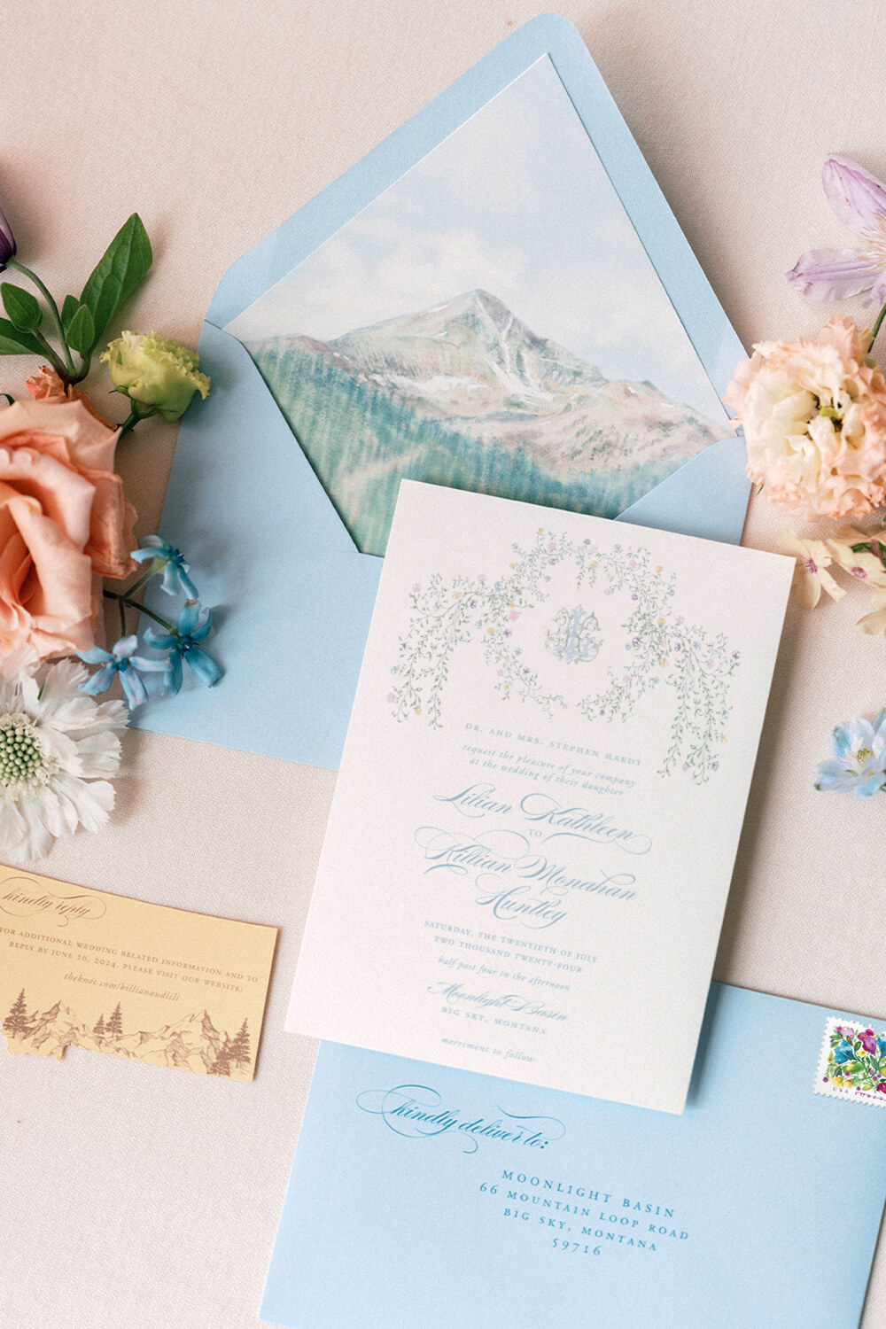 Flatlay of floral wedding invitations featuring a custom watercolor illustration of Lone Mountain as the envelope liner, vintage monogram, and Montana die-cut card.