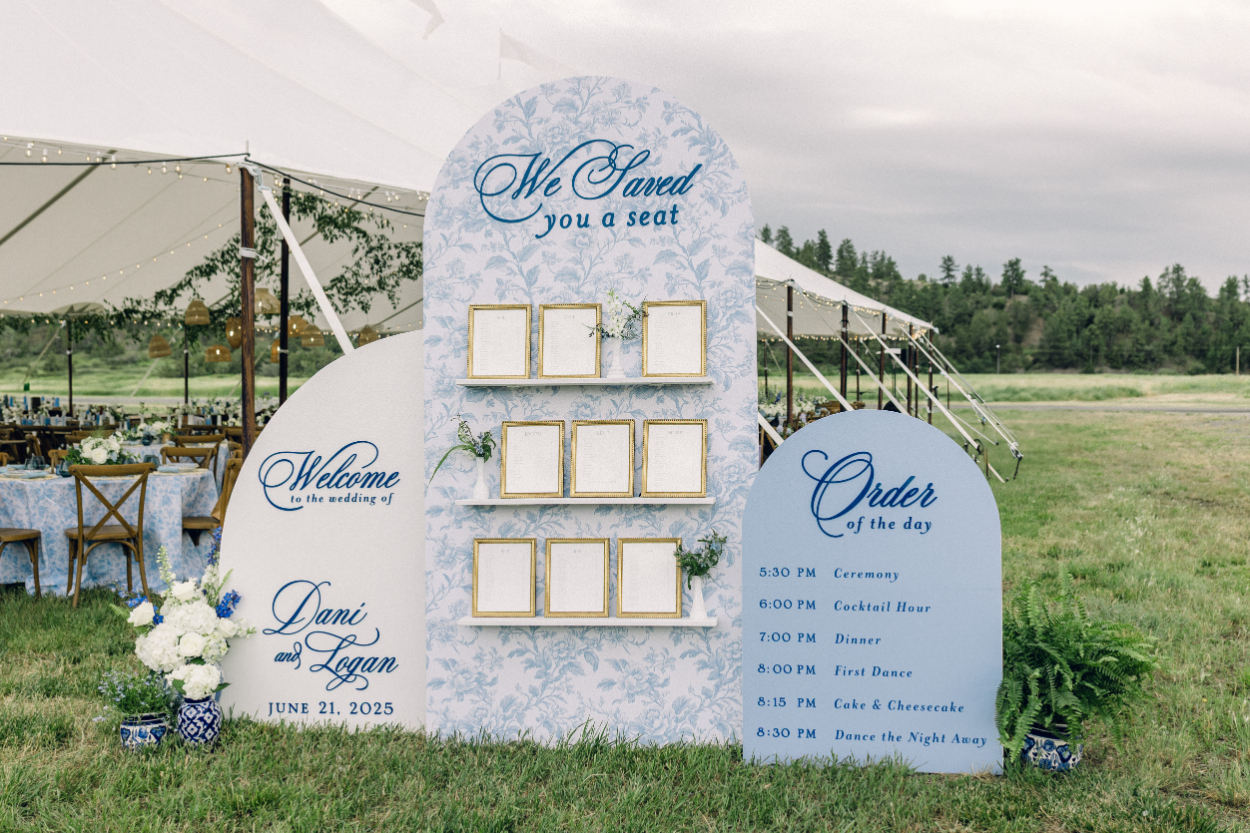 Large outdoor seating display with welcome sign, seating chart, and order-of-the-day signage arranged near a tented reception, helping guests navigate the celebration with clarity and ease.