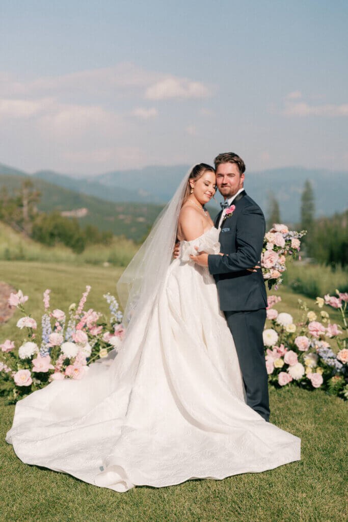 Bride and groom standing together in front of pastel ceremony florals with sweeping mountain views at their Moonlight Basin wedding.