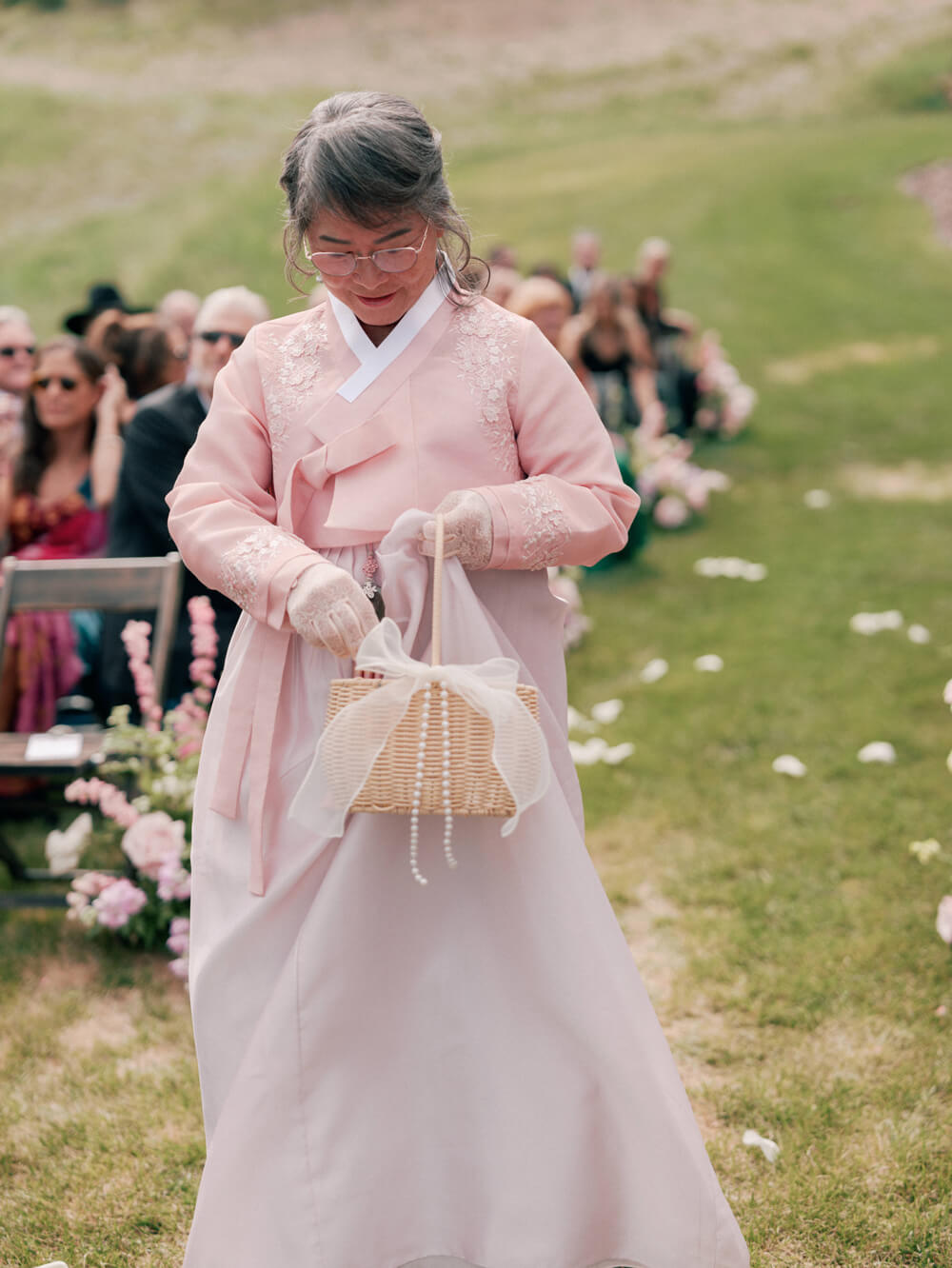 Grandmother serving as flower girl wearing a pastel pink modern hanbok during a Moonlight Basin wedding ceremony in Big Sky, Montana.