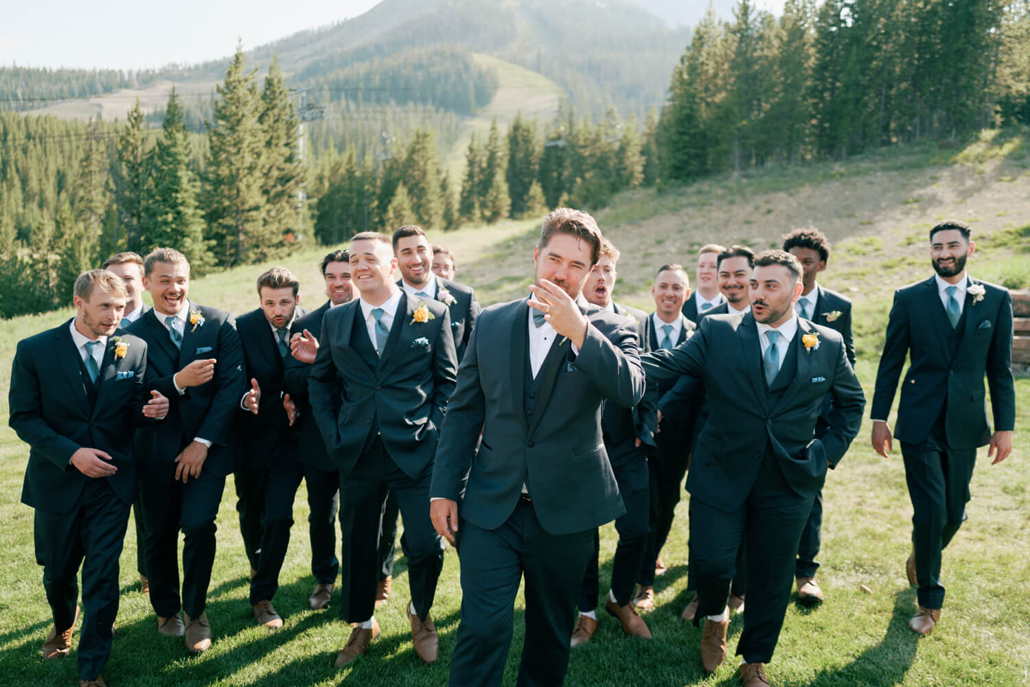Groomsmen in coordinated black suits walking together on a hillside at Moonlight Basin in Big Sky, Montana.
