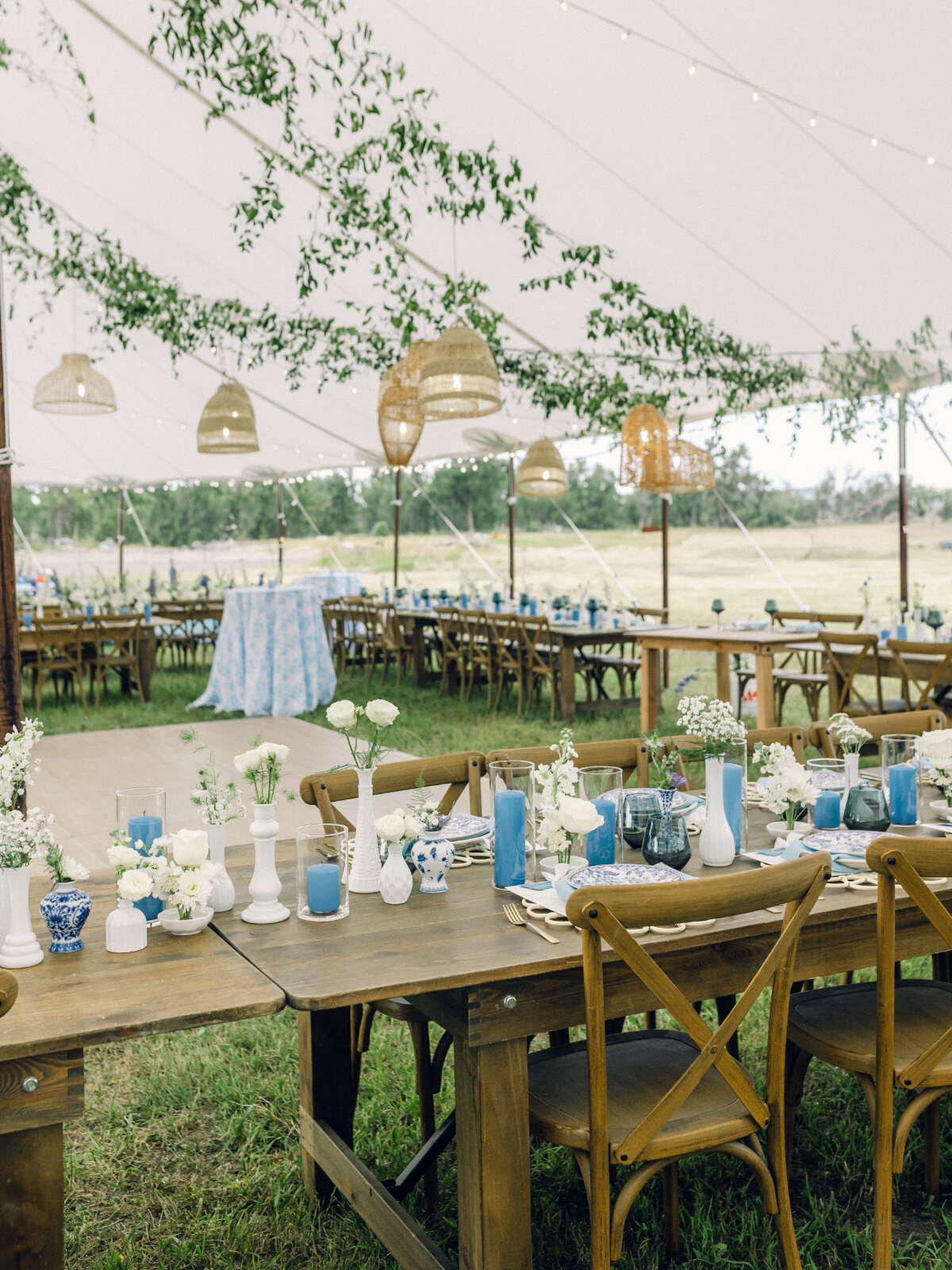 Elegant outdoor reception under a white tent with greenery, blue candles, and florals; an example of how hiring a wedding planner shapes cohesive design.