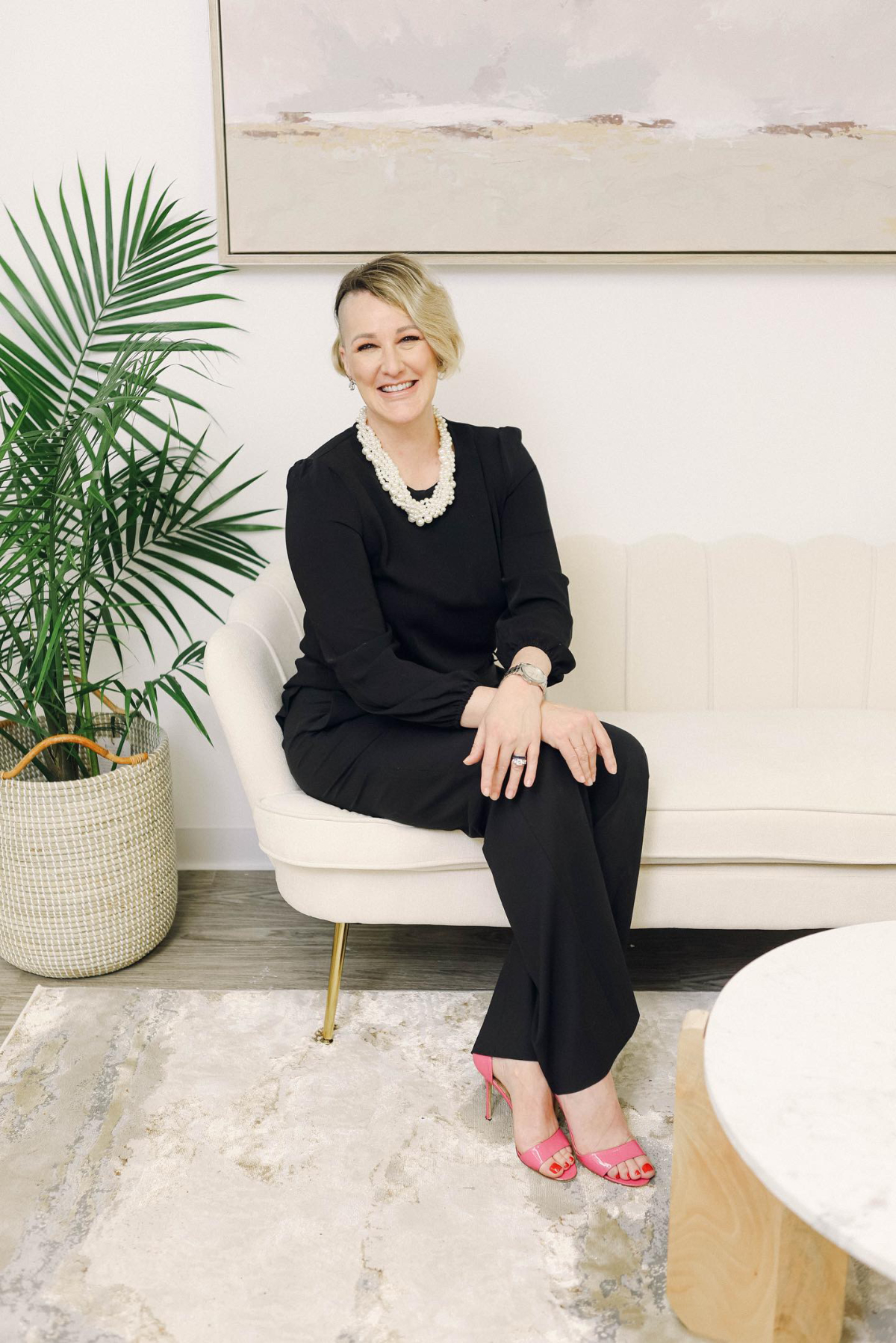 Professional wedding planner seated on a cream sofa in a modern studio with greenery and artwork, illustrating the value of hiring a wedding planner for expert guidance.