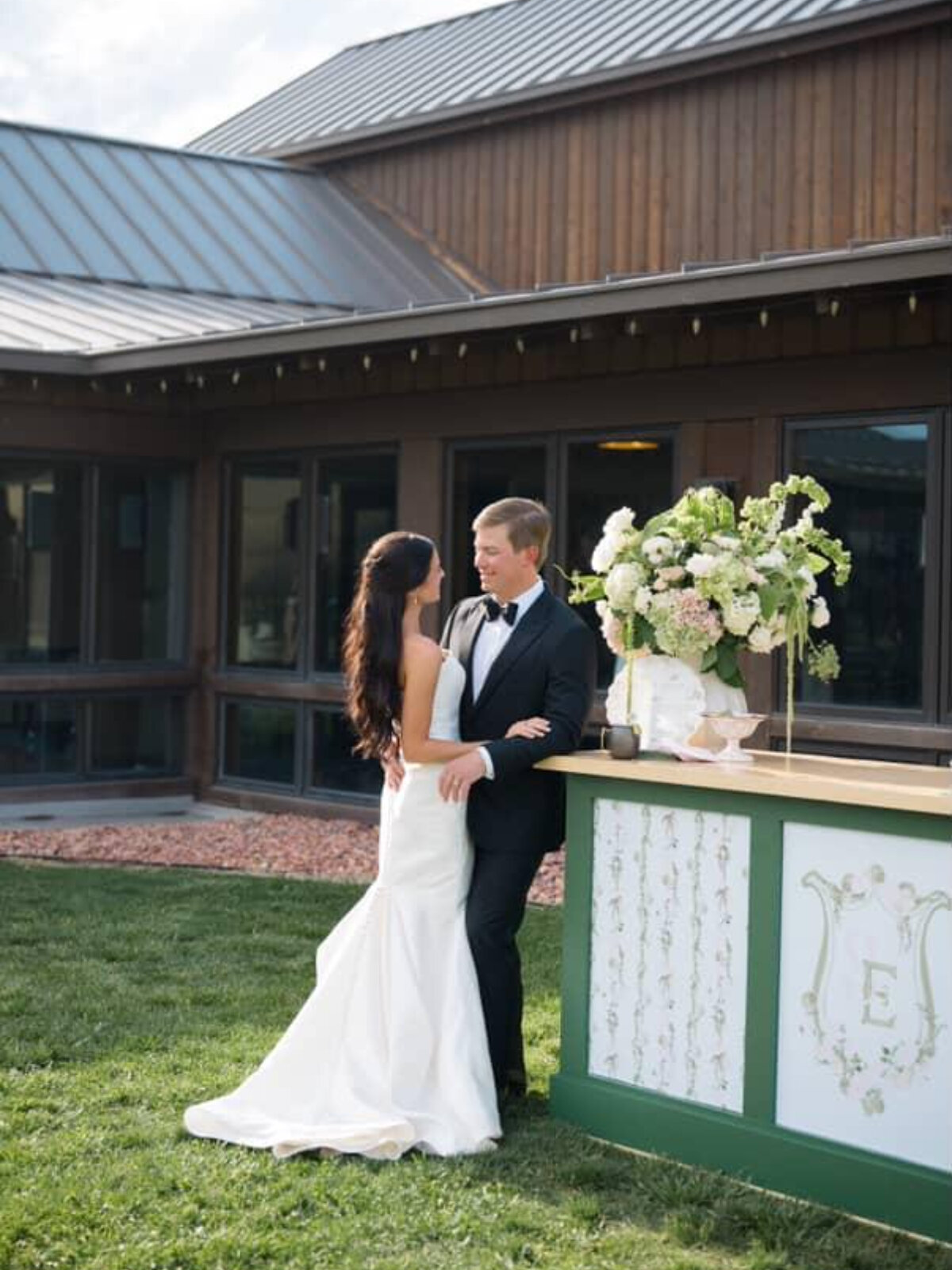 Bride and groom embrace beside a custom floral bar installation during an outdoor wedding, showcasing thoughtful details often guided by hiring a wedding planner.