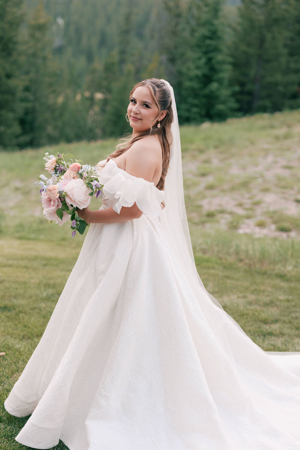 Bride wearing an off-the-shoulder white wedding gown with a soft A-line skirt, photographed outdoors at a mountain wedding in Big Sky, Montana.