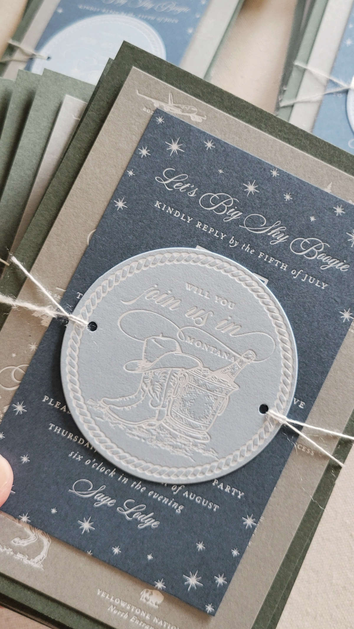 Western-inspired embossed invitation card stack with rope detailing and star accents for a Sage Lodge, Montana wedding celebration.