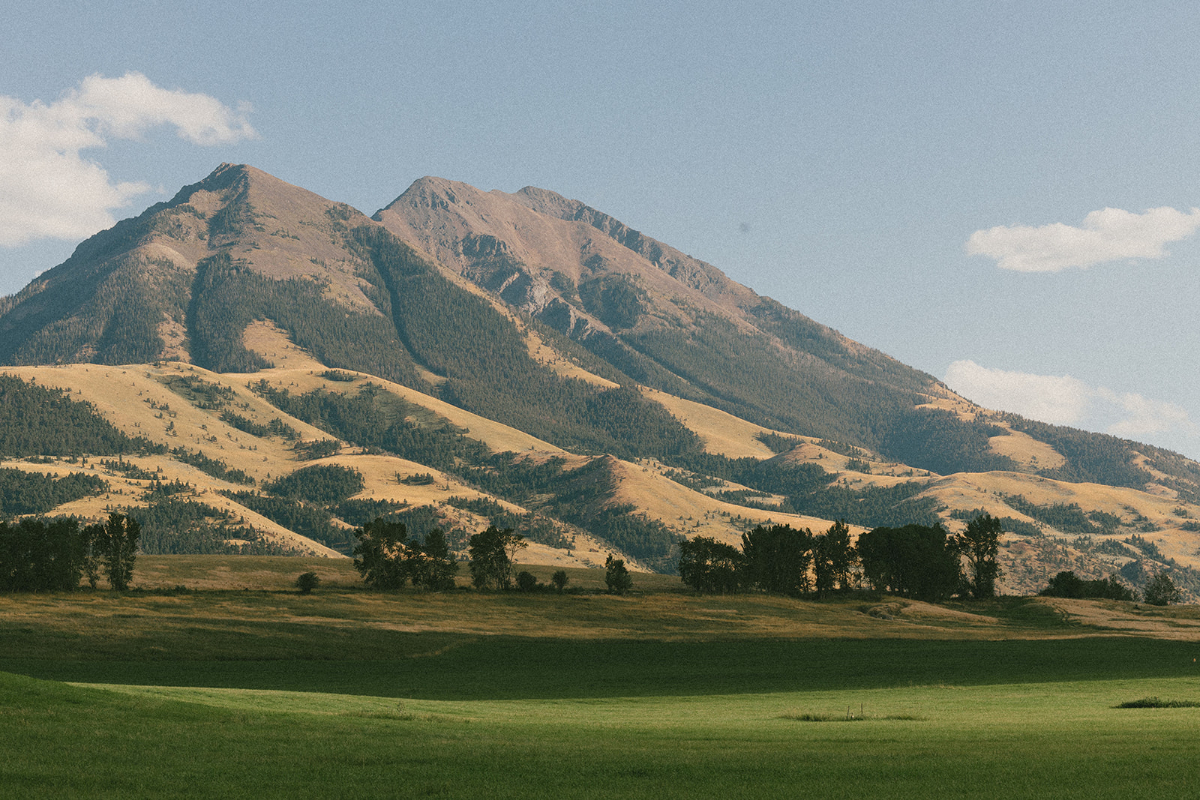 Scenic mountain landscape with rolling golden hills and green pastures at a Sage Lodge, Montana wedding location beneath a clear summer sky.