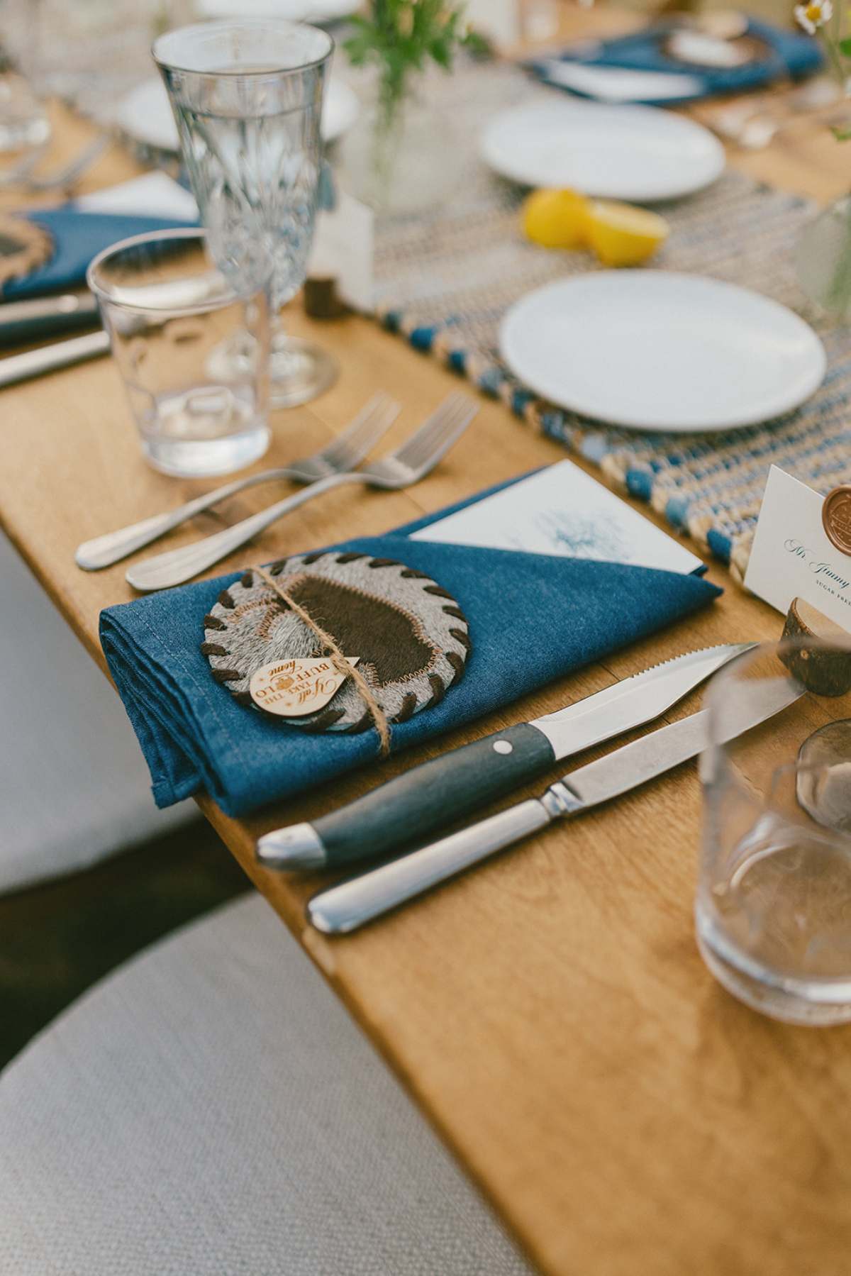 Rustic place setting with blue napkin, leather coaster, and twine detail at a Sage Lodge, Montana wedding reception.