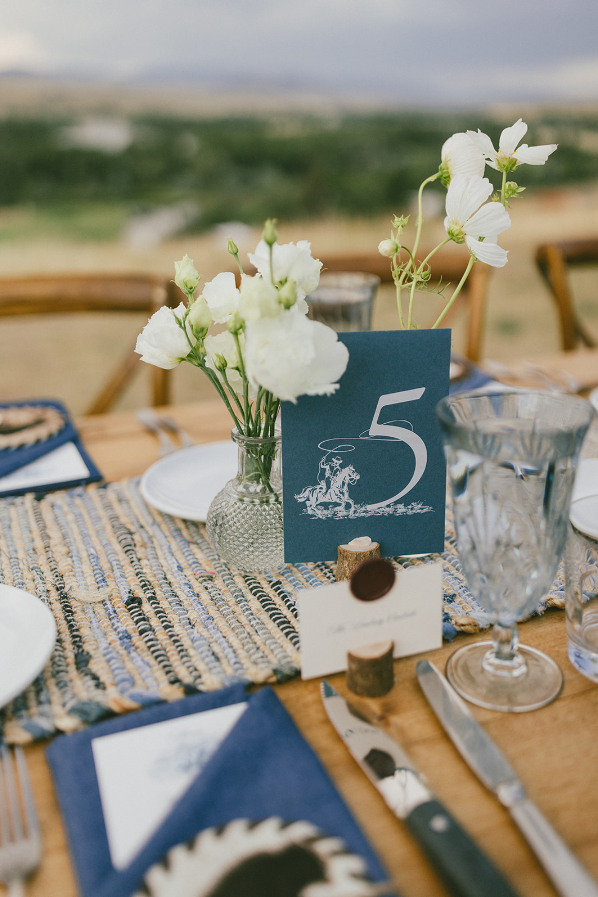 Table centerpiece with white flowers and navy table number featuring cowboy illustration at a Sage Lodge, Montana wedding.