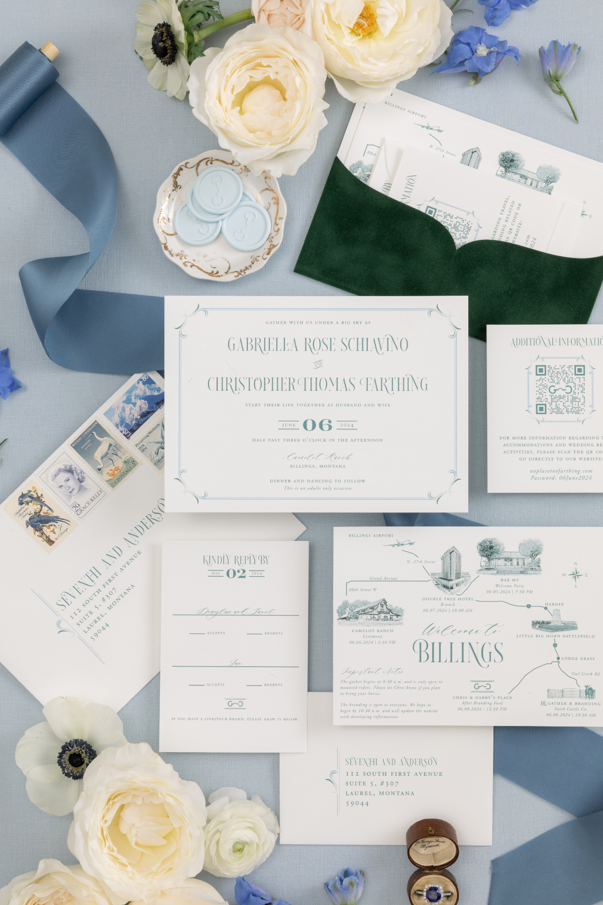Flat lay of a blue and green illustrated wedding invitation suite with venue map, velvet envelope, stamps, ribbon, and white and blue flowers on a pale blue surface | wedding invitation questions