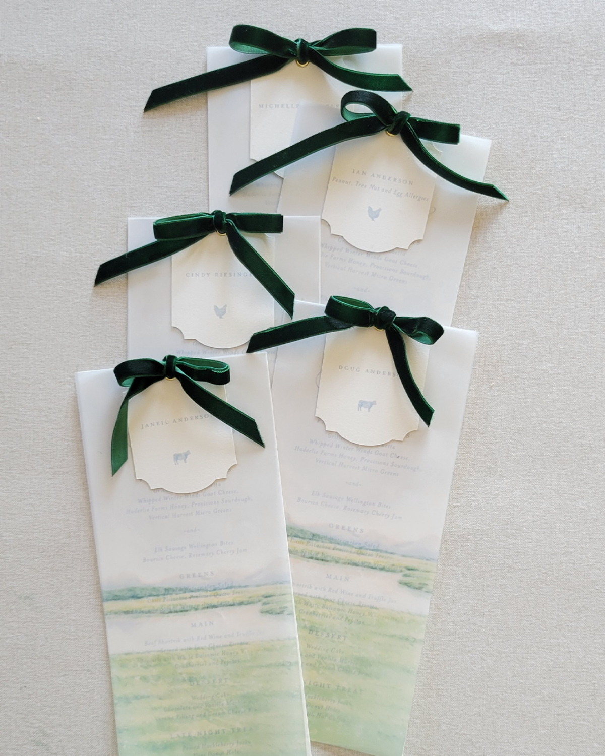 Choosing Your Wedding Invitation Style 12 Long menu cards tied with dark green velvet bows, arranged neatly on linen, blending watercolor details with a timeless wedding invitatin style.