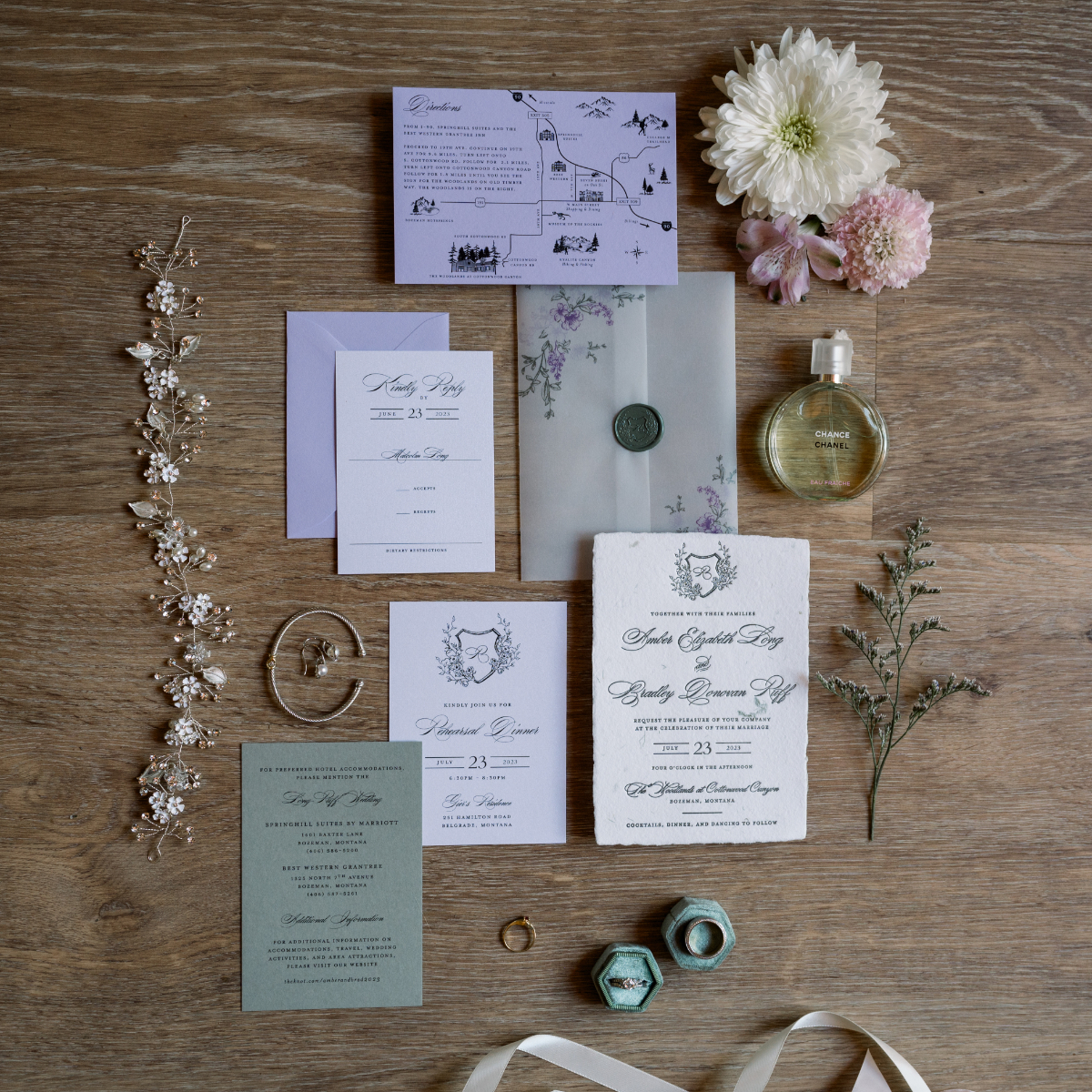 Choosing Your Wedding Invitation Style 5 Flat lay of elegant wedding invitations and paper goods arranged on a wooden surface, styled with flowers, greenery, rings, jewelry, wax seal envelope, perfume bottle, and hair accessories.