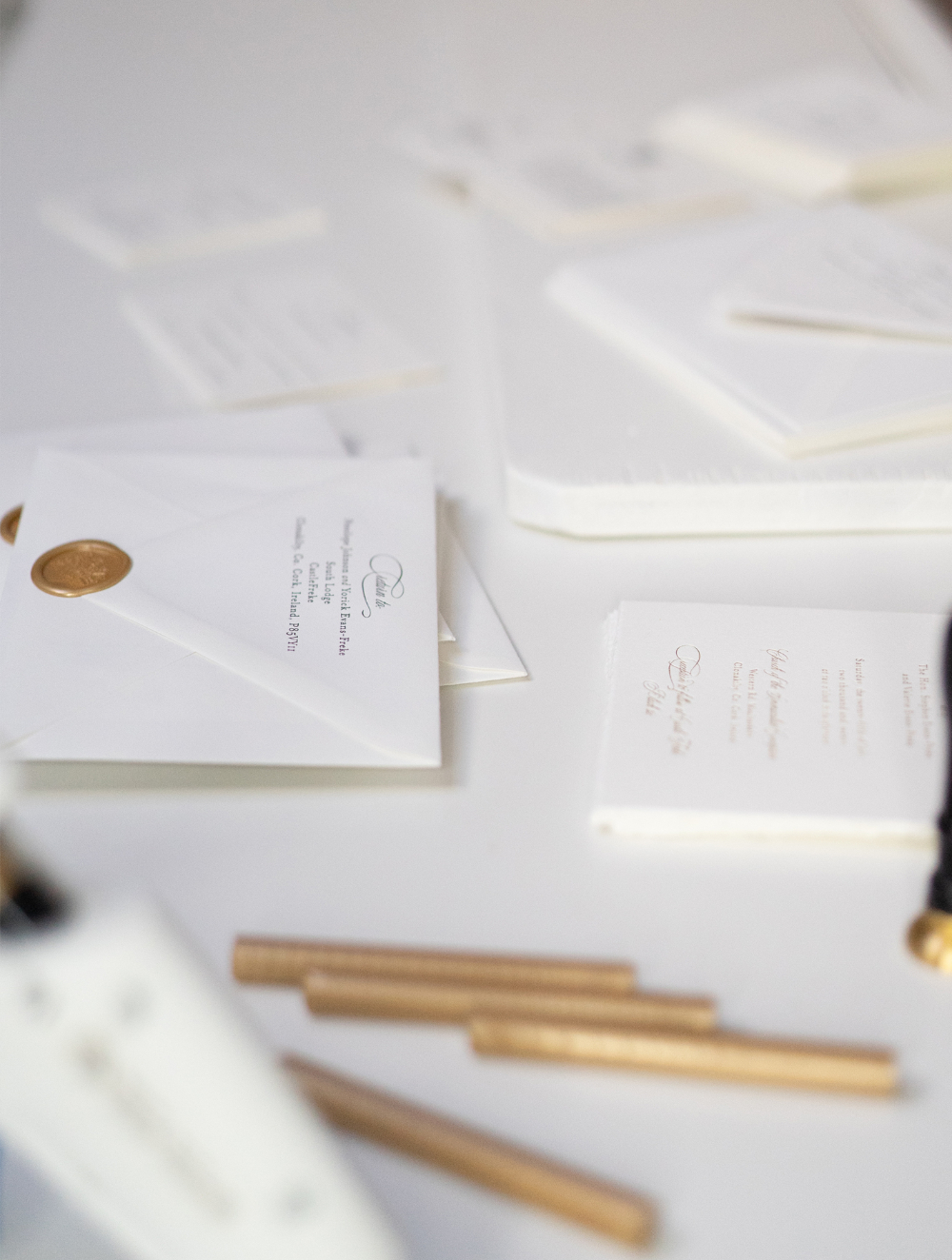 Side view of letterpress wedding invitations stacked on marble alongside sealing wax and envelopes. The scene emphasizes artisanal production, texture, and the behind-the-scenes care involved in creating luxury wedding invitations.
