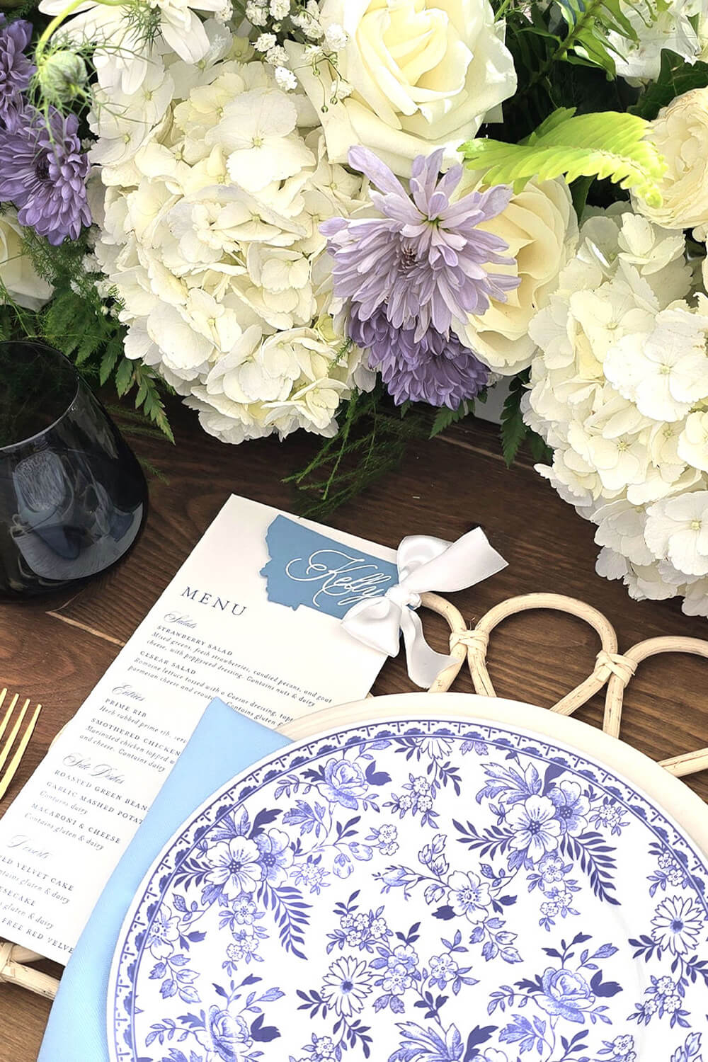 Summer wedding tablescape in blue and white shades with a blue floral salad plate and wedding menu with guest place card in the shape of Montana.